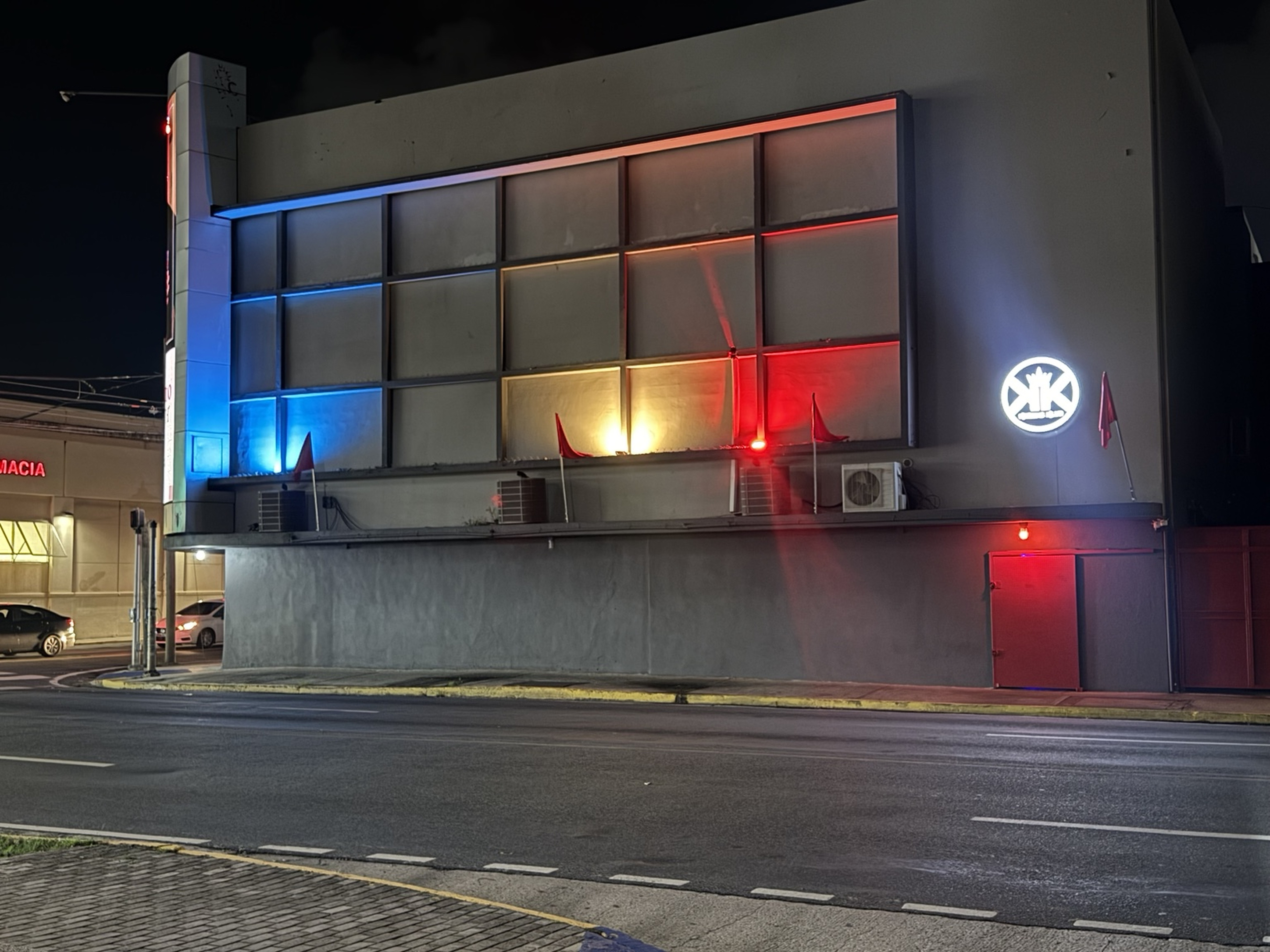 Fachada nocturna — Vista frontal real con la iluminación arquitectónica de Kweens encendida.